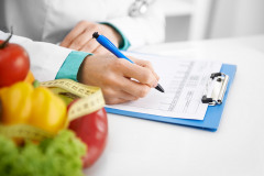 Doctor nutritionist writing case history in the office. Young woman dietitian prescribing recipe.